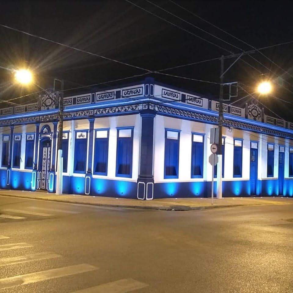 Fachada de casarão histórico em azul e branco, iluminada à noite