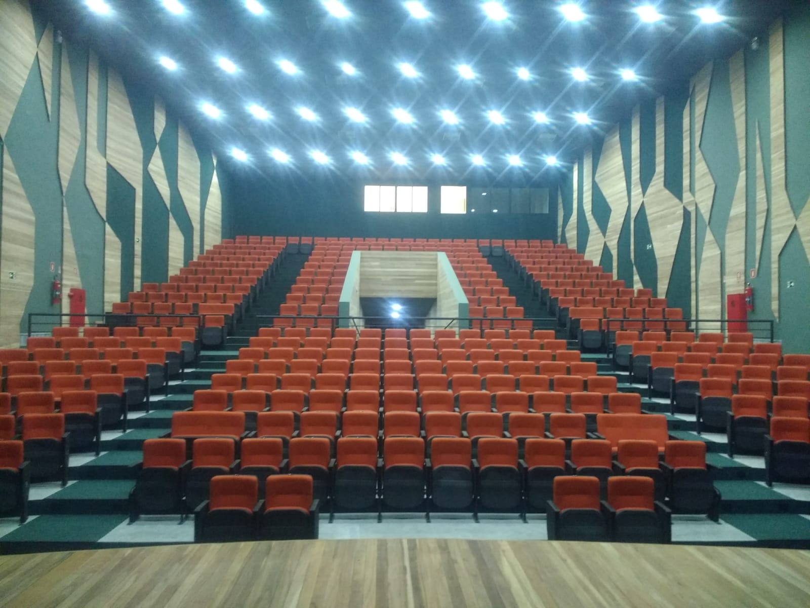 Plateia escalonada de teatro com poltronas laranja e painéis acústicos em madeira
